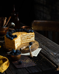 Delicious homemade cut of russian honey cake medovik with white cream, blue and black berries on top