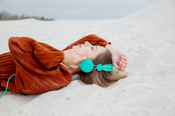 Young woman in burgundy color blouse with headphones lying down