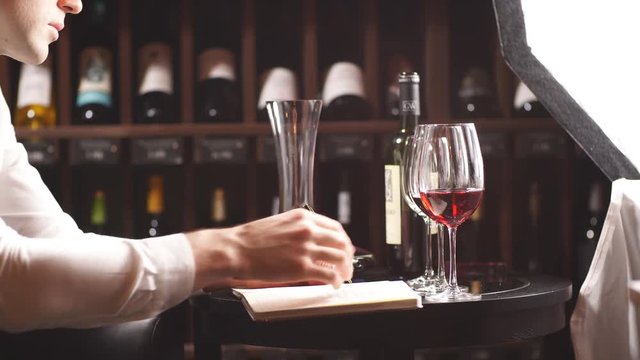 Professional male cavist examines the bottles with wine in wine shop, holding wonderful sample, ready to speak out about this wine to customers
