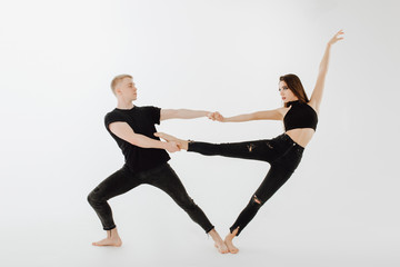 Fototapeta premium Professional Caucasian Performer Couple Posing. Beautiful Female Dancer Wear Black Denim. Blond Male Dancer Hold Partner Pointe Leg. Contemporary Duet Looking in Eye Isolated on White Background