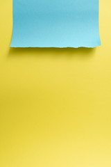 Vertical yellow-blue paper background. A piece of blue paper with torn edges at the top against the background of a sheet of yellow paper
