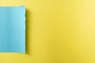 Yellow-blue paper background. A piece of blue paper with torn edges on the left of the background of a sheet of yellow paper