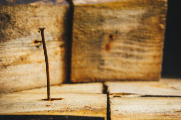 Old long rusty curve nail hammered into a wooden bar on a rustic wooden background close-up. macro