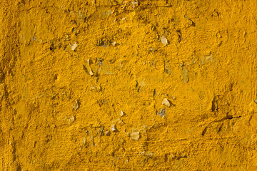 an old shabby bright yellow wall with deep relief, scraps of paper and cracks with shadows. rough surface texture