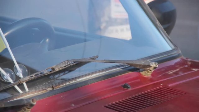 Ukrainian national flags attached to auto windshield glass under car wipers. Old fashioned red colored soviet automobile Zhiguli Vaz Lada in sunny spring day. Ukraine, circa spring 2019