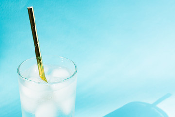 Close up of pure water with ice and paper straw in transparent glass and sun glare on blue  background.