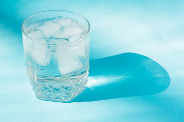 Close up of pure water with ice  in transparent glass and sun glare on blue  background.