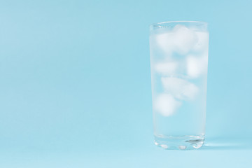 Close up of pure water with ice in tall transparent glass with copy space on blue  background.