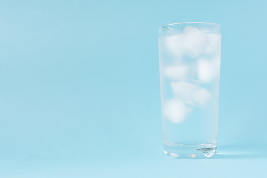 Close up of pure water with ice in tall transparent glass with copy space on blue  background.