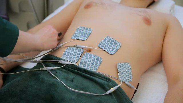Electrostatic massage procedure. Female doctor attaching electrodes close up on patient's belly