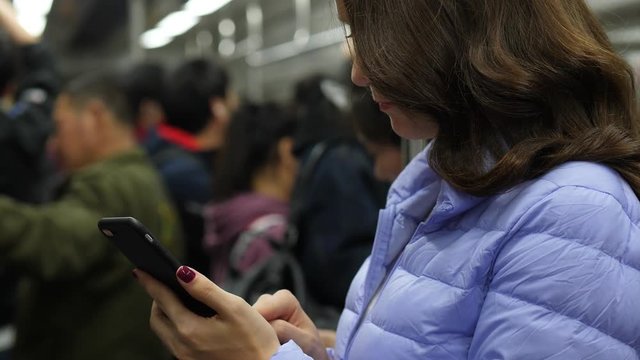 Woman quickly swipe smartphone, looking through photos while ride at subway in Beijing, portrait shot with blurred background. Passengers stay holding handrails, train shake during ride