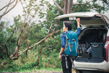 Man traveler sitting on hatchback car with mountain.  Travel concept with big car against sunset and mountains. Man driving car on to the mountains. Traveler with backpack.