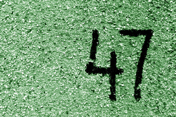 Number 47 on cement wall in stencil in green tone.