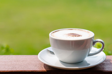 Hot coffee placed on the wooden table in early morning with copyspace, white cup and silver spoon. The green background with defocus effect.