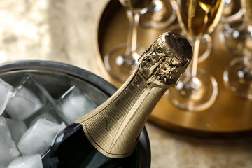 Bottle of champagne in bucket with ice cubes on table, closeup