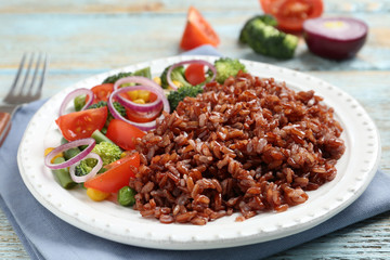 Plate of cooked brown rice with vegetables on table, closeup