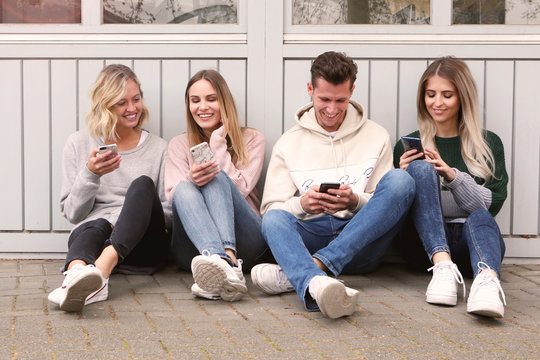 Vier junge Leute mit Handys sitzen an eine Wand gelehnt