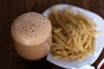 Close-up of a dark beer froth, french fries in the background. Men's set to watch a football match or a party
