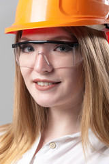 Portrait of a young attractive woman with blond hair in orange helmet on a neutral gray background.