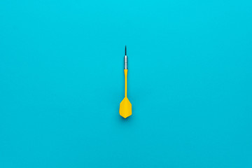 minimalist photo of yellow plastic dart with metal tip on blue background