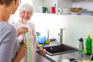 Senior woman/grandmother cooking in a modern kitchen with her grand-daughter, tasting a green smoothie (shallow DOF; color toned image)