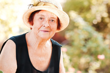 Smailing mature woman 70-80 year old wearing straw hat in garden. Looking at camera. Summer season.