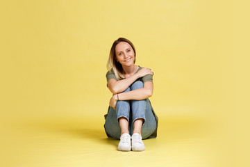 Obraz na płótnie Canvas Cute young female student with big brown eyes sits on the floor on a yellow background. Place for text