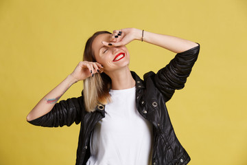 Portrait of young smiling woman with red lips covered eyes to see surprise. Funny excited girl with ombre and black leather jacket on yellow background.