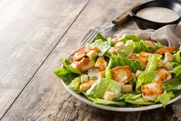 Caesar salad with lettuce,chicken and croutons on wooden table. Copyspace
