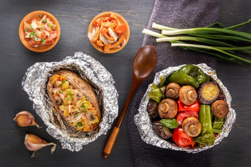 Baked vegetables in foil - tomatoes, eggplants, peppers and baked potatoes with bacon, onions on a gray wooden table. Top view