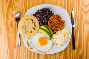 Venezuelan breakfast of arepa, fried egg, black beans, mechada meat, white cheese and avocado