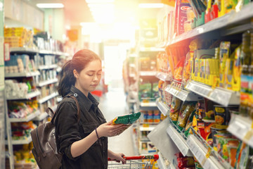A young pretty woman holds a grocery cart and carefully chooses the products in the store. Light