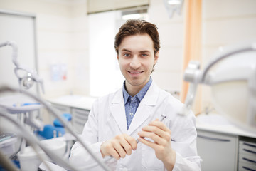 Waist up portrait of smiling dentist looking at camera while posing in office holding bur machine, copy space