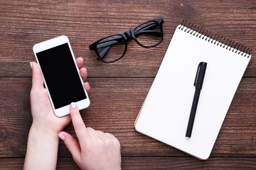 Smartphone in female hands with notebook and glasses on wooden table
