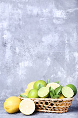 Lemons and limes with green leafs in basket on grey wooden table