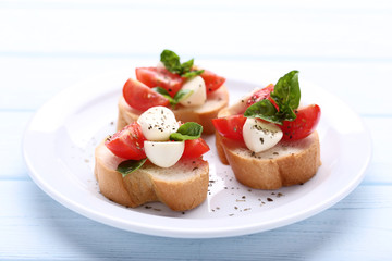 Bruschetta with mozzarella, tomatoes and basil leafs on wooden table
