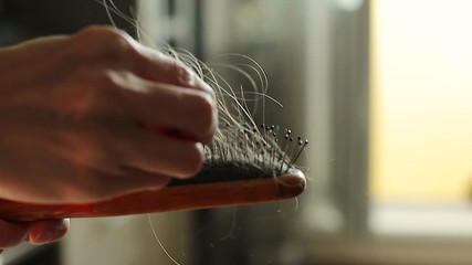 A woman's hand holding a comb with hair. The concept is the problem of hair loss. Close-up of slow motion
