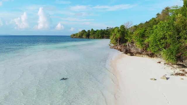 Aerial slow motion: woman walking on tropical island turquoise water white sand beach, Tomia Island, Wakatobi marine national park, Indonesia, paradise travel destination