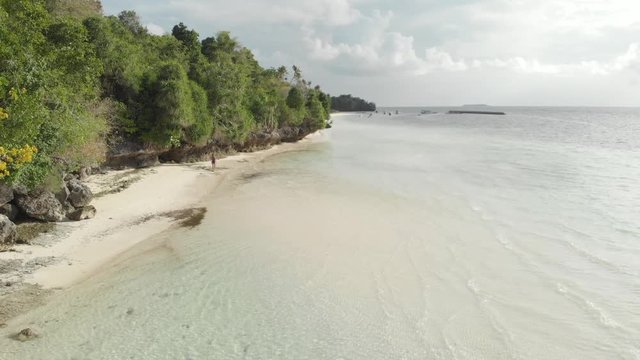 Aerial: woman walking on tropical island turquoise water white sand beach, Tomia Island, Wakatobi marine national park, Indonesia, Native cinelike D-log color profile