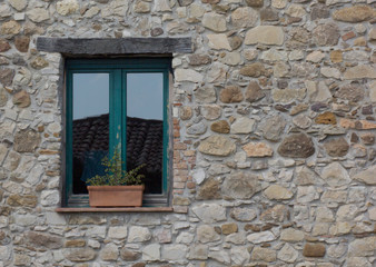 one window on the stone house wall with flower pot on the window sill 