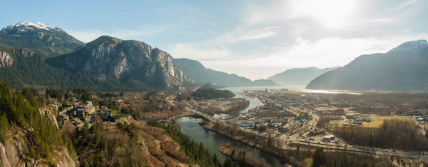 Aerial panoramic view of a small town with Chief Mountain in the background during a sunny day. Taken in Squamish, North of Vancouver, British Columbia, Canada.