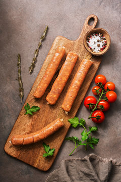 Raw sausages with cherry tomatoes and spices on a cutting board, rustic brown background. Top view, flat lay