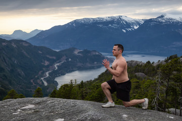 Naklejka na ściany i meble Fit and Muscular Young Man is doing exercises on top of the Mountain during a cloudy sunset. Taken on Chief Mountain in Squamish, North of Vancouver, BC, Canada.