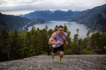 Fit and Muscular Young Man is Running up the Mountain during a cloudy day. Taken on Chief Mountain in Squamish, North of Vancouver, BC, Canada.