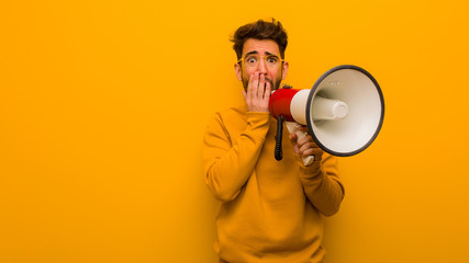 Young man holding a megaphone very scared and afraid hidden