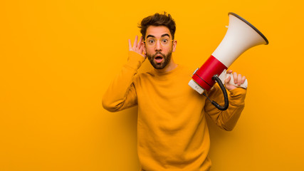 Young man holding a megaphone try to listening a gossip - obrazy, fototapety, plakaty