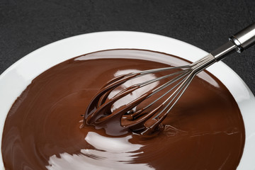 Macro of Melted milk or dark chocolate swirl in plate and whisk on concrete background