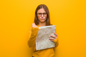 Fototapeta premium Young pretty caucasian woman showing fist to front, angry expression. She is holding a map.