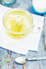 Fresh chamomile tea in a glass cup on a wooden table, chamomile blossoms in a cup, healthcare and healthy eating concept