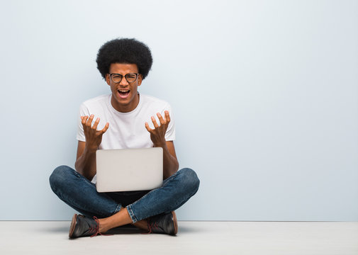 Young Black Man Sitting On The Floor With A Laptop Angry And Upset